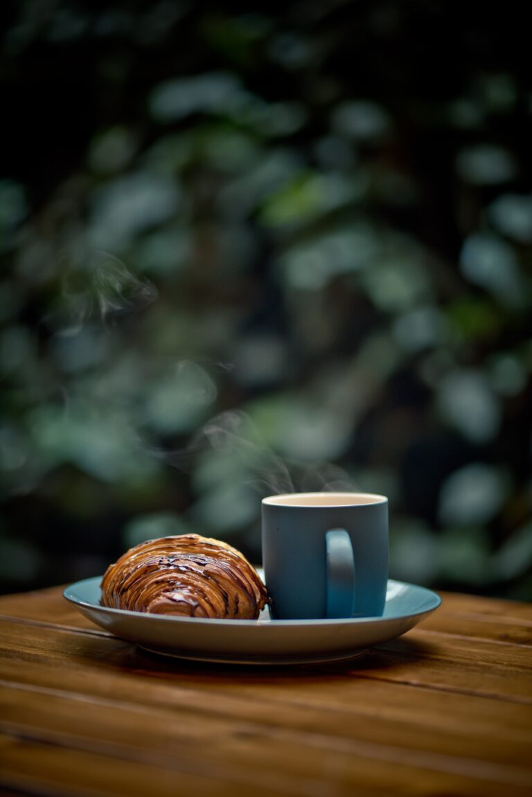 Steaming mug with chocolate croissant on plate